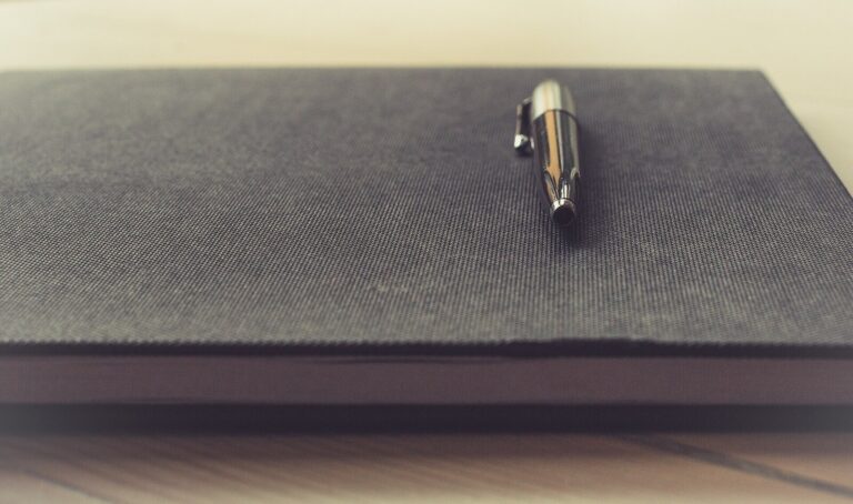 Zamkniety czarny notes z metalowym dlugopisem na biurku