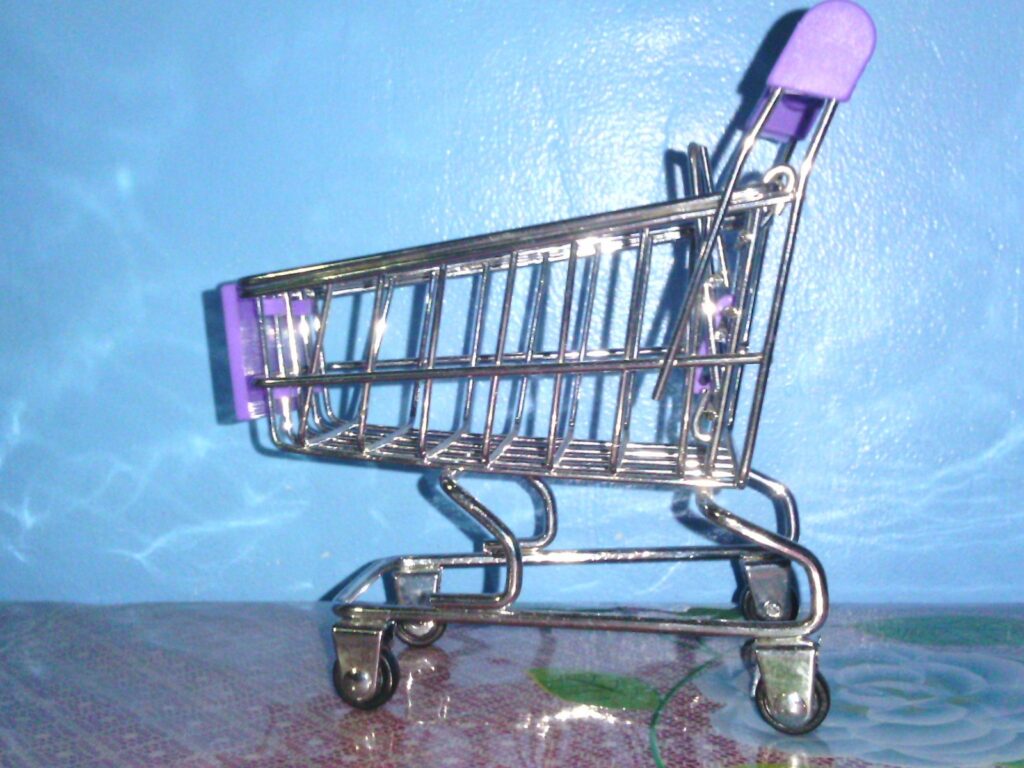 Miniaturowy metalowy wózek sklepowy z fioletowym uchwytem na niebieskim tle